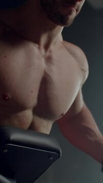 Focused shirtless athlete training upper body strength on gym equipment, highlighting muscular chest, shoulders, and arms in dramatic low key fitness lighting