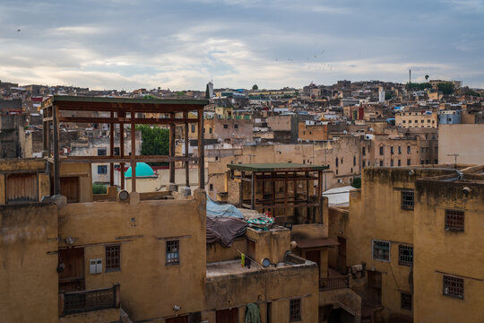 Elevated architectural perspective overlooking weathered residential rooftops, timber pergola structures, and the dense ancient urban fabric inside the medina of Fes, Morocco