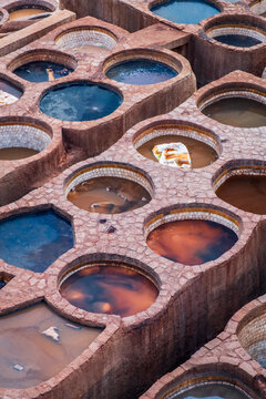 vertical aerial close up of the textured circular stone basins filled with natural processing liquids inside the historic leather tanneries of Fes, Morocco