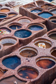 vertical aerial close up of the textured circular stone basins filled with natural processing liquids inside the historic leather tanneries of Fes, Morocco