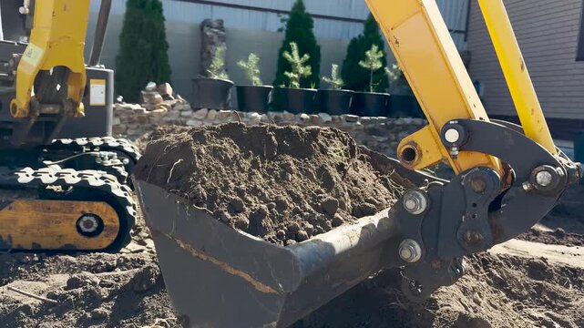 Bucket tracked excavator levels the ground in backyard house. Mini excavator scoops up soil, construction work supervised engineer. Earthworks being carried out using excavator. Building, Earthmoving