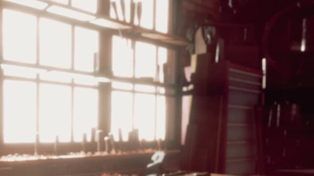 Warm sunlight streams through large windows in a cluttered workshop. Tools are scattered across a workbench, surrounded by shavings from wood projects created within these walls.