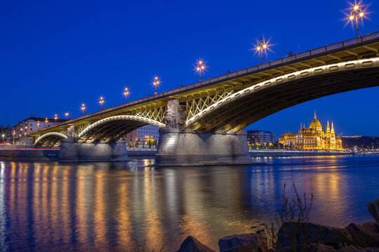 Margit Bridge and Hungarian Parliament with glowing reflections on the Danube at blue hour, Budapest