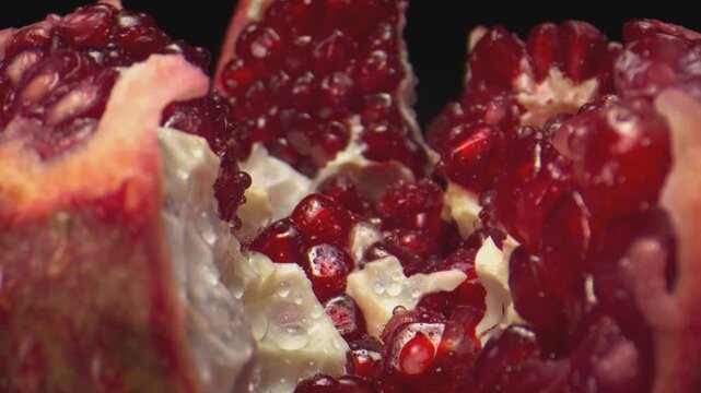 Macro closeup of pomegranate arils and white pith with glossy red juice, warm dramatic light, and dark background showing juicy seeds