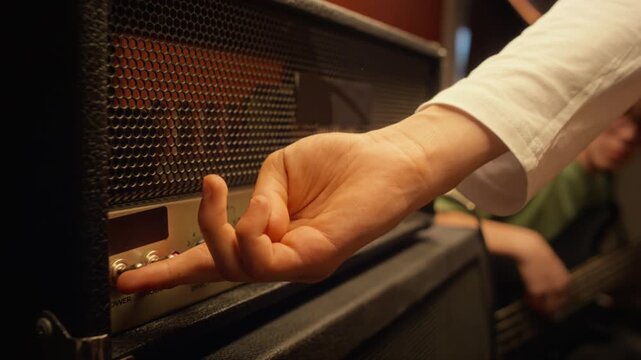 Caucasian teenage musician plugging audio cable into guitar amplifier and turning power switch on in rehearsal room. Clip suitable for music education, youth creativity, audio gear advertising