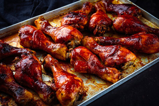 Traditional oven roasted barbecue chicken drumsticks with hot honey chili sauce served as close-up on rustic metal baking tray
