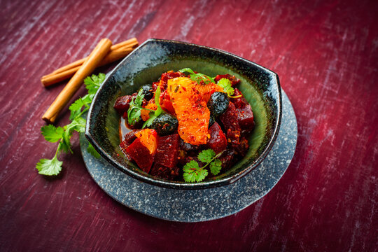 Vegetarian vegetable and fruit salad with red beets, orange and black dried olves served as close-up in a design bowl