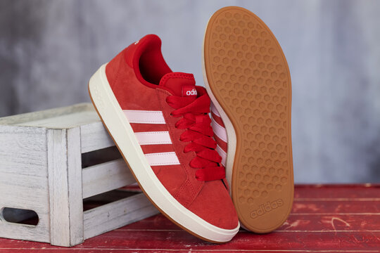 Red Adidas sneakers display a striped side beside an upright patterned outsole.