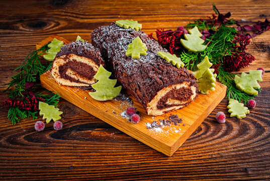 Traditional French homemade christmas cake b&ucirc;che de no&euml;l, yule log with sponge cake and chocolate buttercream ganache served as close-up on a rustic wooden board