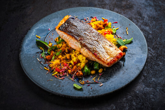 Fried salmon fish fillet with saffron rice, nuts and vegetable served as close-up on a design plate