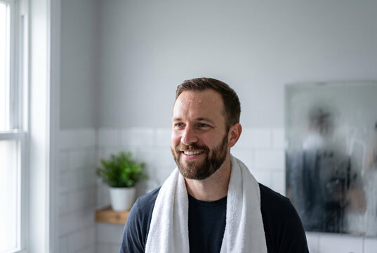 Smiling man with a freshly washed face and towel in a bathroom