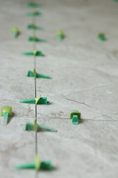 A series of green spacers are aligned on a tiled floor. These spacers help keep tiles evenly spaced for grout application in a renovation project. The work area is indoors.