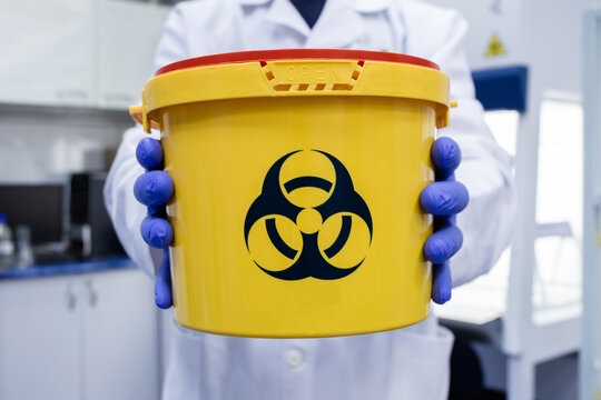 A scientist holds a large biohazard container in front of them. Caution when handling hazardous biological contamination.