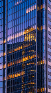 Warm lit offices glowing inside reflective glass tower facade at dusk in downtown financial district