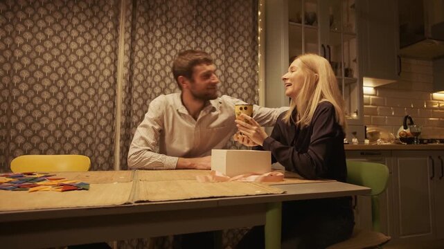 Young couple celebrating a special occasion at home, with the man gifting a beautiful goblet to his delighted wife, who opens the box, kisses him, and admires her new surprise present