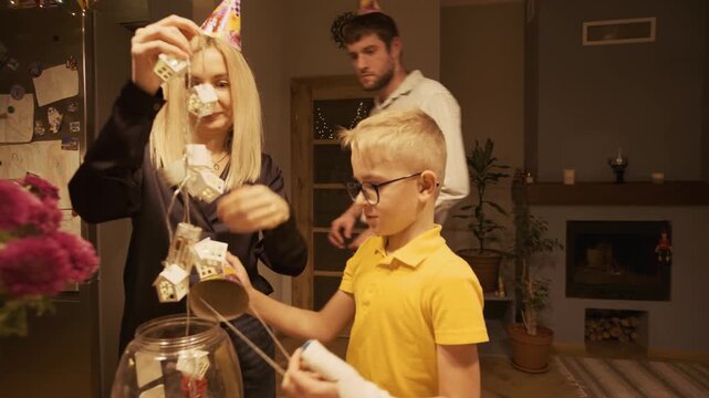 Young caucasian family, including mother, father, and son with a cast on his arm, joyfully preparing for a birthday party by untangling festive house-shaped string lights together