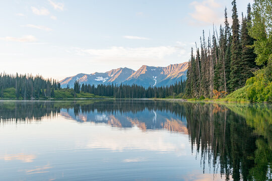 Reflections of mountains in calm lake under blue sky with evergreen trees on sunny day