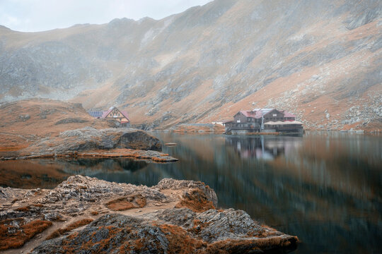 Atmospheric foggy morning at Balea Lake in the Fagaras Mountains, Romania, with mist rolling over the dramatic autumn mountain peaks and calm water.