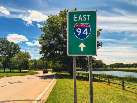 Green Interstate 94 East highway sign along a paved road near a pond and grassy field at the New Buffalo Welcome Center near the Michigan state line.