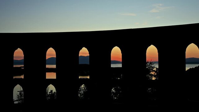 Repeated stone arches frame warm evening sky and distant coastal water near Oban, Scotland.