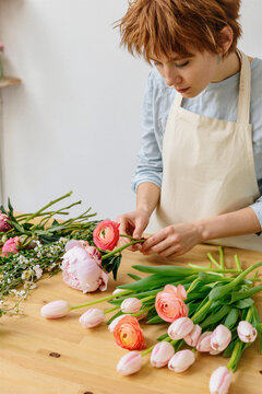 Young florist placing a ranunculus into a pastel spring bouquet