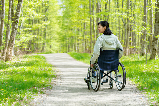 Young woman in a wheelchair rolling along a forest trail in spring