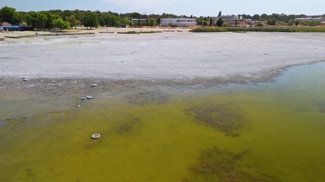Drone view of the exposed muddy lakebed and algae-covered shallow water at Lake Velence in Velence, Hungary, showing an unusually low shoreline during summer drought.
