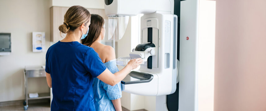 Professional healthcare worker wearing a mask positions a female patient for a mammography examination using specialized medical equipment to screen