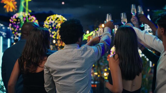 Close up of people watching fireworks and clinking champagne flutes during New Year's Eve on rooftop terrace, with group of partygoers doing celebratory toast, enjoying New Year celebration.