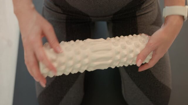 Close up shows someone hands holding and rolling over cylindrical bumpy textured object for muscle relaxation or physical activity. person wears form fitting athletic wear with visible