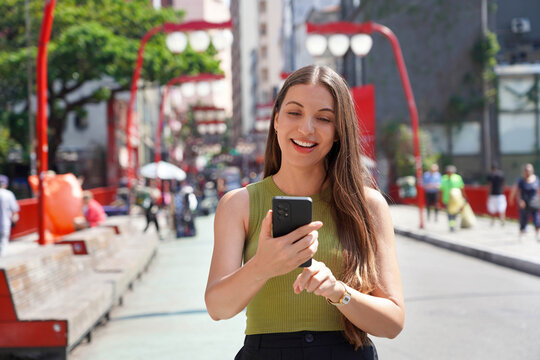 Portrait of smiling woman using smartphone walking in Liberdade neighborhood in Sao Paulo, Brazil