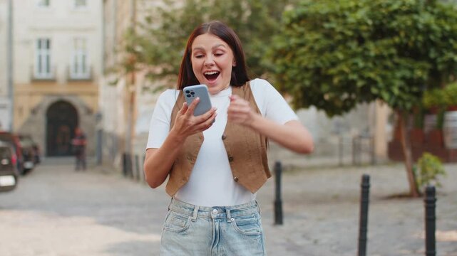 Caucasian young woman using smartphone typing texting social media messages e-mail looking for a way on map in mobile navigator app outdoors. Smiling girl standing on city street. Town lifestyles