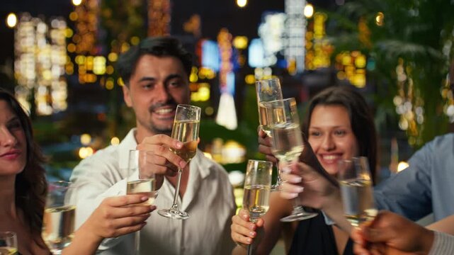 Close up of smiling people enjoying luxury lifestyle, drinking champagne on rooftop terrace, with cheerful men and women mingling at upscale nightlife party late at night, clinking wine glasses.