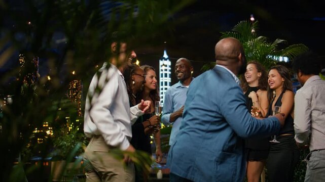 Happy friends dance together at an upscale rooftop party, while upbeat partygoers enjoy loud music, clubbing and having fun late at night in an outdoor nightlife setting above city lights.
