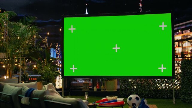 Isolated screen mockup in cozy rooftop viewing area arranged with football props; blank display panel enables sports broadcasting during outdoor watch party above the city skyline.