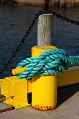 Fototapeta premium Turquoise mooring rope tied around yellow harbor bollard