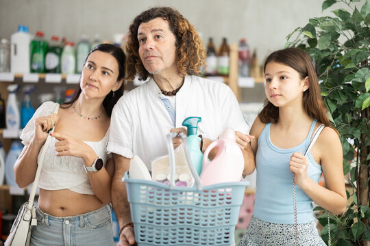 Happy friendly family holding basket full of cleaning products and toiletries while shopping together in home care store