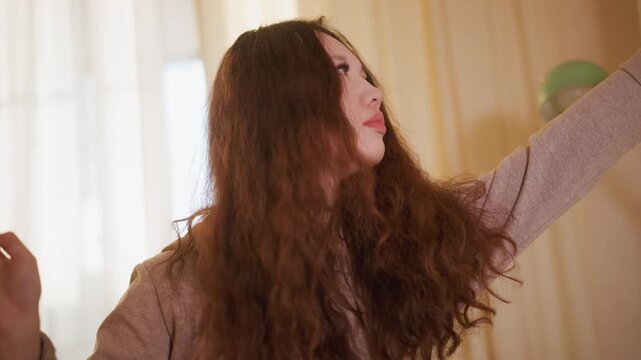 Woman with long curly hair examines tiny object held near her face. Soft lighting illuminates scene creating warm tones and highlighting details of both subject and background