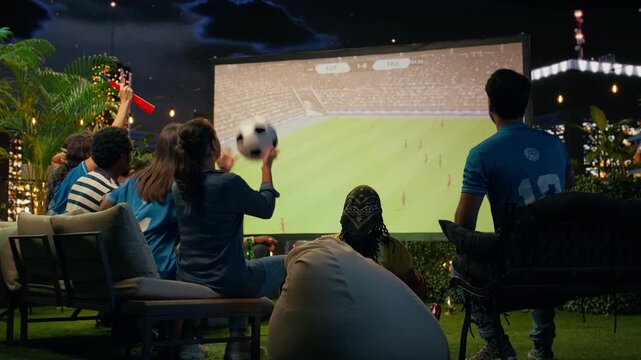 Upset football supporters annoyed by goal received while watching rooftop match projection; dejected fans reacting with negative emotion to own goal during soccer broadcast watch party.