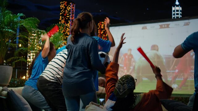 Spectators look dejected during a live football match projected on a rooftop terrace screen as devoted supporters react to their team's loss.