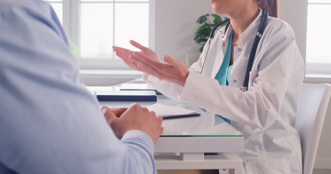 Female doctor talking with male patient sitting on workplace at the desk in clinic. Physician giving consultation a man during medical examination. Medicine and treatment concept. 4k video.