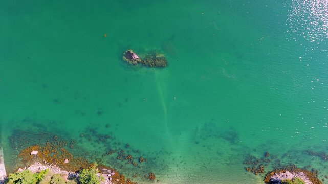 Top-down aerial view of clear emerald coastal waters showing submerged rocks, seaweed beds, and a boat ramp along the shore in Maine.