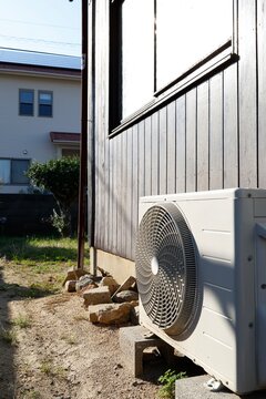 日光に照らされたエアコン室外機。木板の外壁脇に設置。