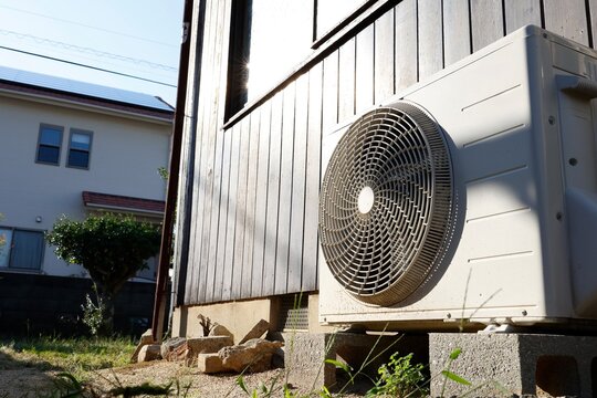 日光に照らされたエアコン室外機。住宅外壁脇に設置
