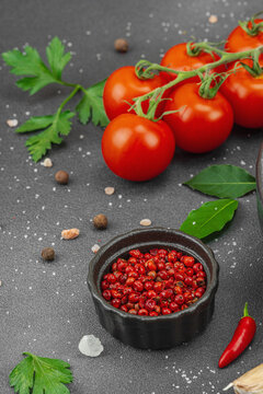 Culinary background with vine tomatoes, garlic, spices, salt, and herbs scattered on a dark surface