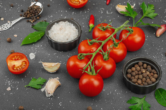 Culinary background with vine tomatoes, garlic, spices, salt, and herbs scattered on a dark surface