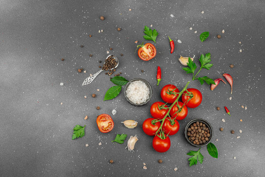 Culinary background with vine tomatoes, garlic, spices, salt, and herbs scattered on a dark surface