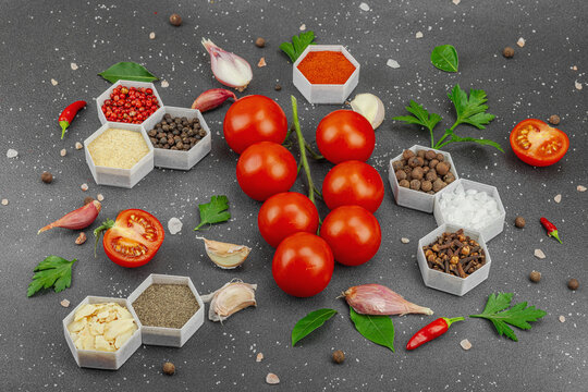 Culinary background with vine tomatoes, garlic, spices, salt, and herbs scattered on a dark surface