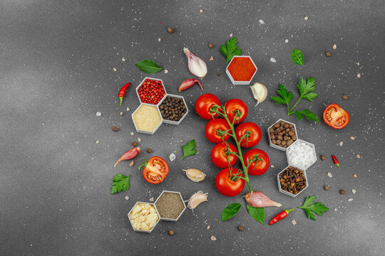 Culinary background with vine tomatoes, garlic, spices, salt, and herbs scattered on a dark surface