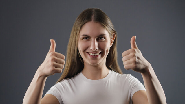 Young woman smiling and showing thumbs up gesture, indicating approval and success